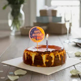 GRUB Singapore Signature Basque Burnt Cheesecake with a lit candle and 'Happy Birthday' topper.