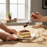 GRUB Singapore Tiramisu tray slice with coffee soil topping, served on a white plate with a spoon adding more topping.