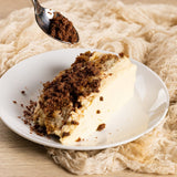 GRUB Singapore Tiramisu tray slice with coffee soil topping on a white plate, served with a spoon.